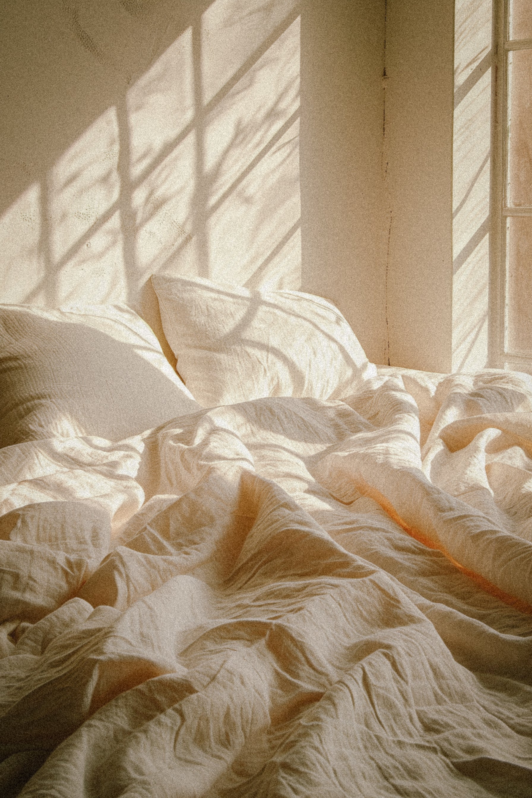 Sunlight over soft white sheets symbolizing restful, rejuvenating beauty sleep.